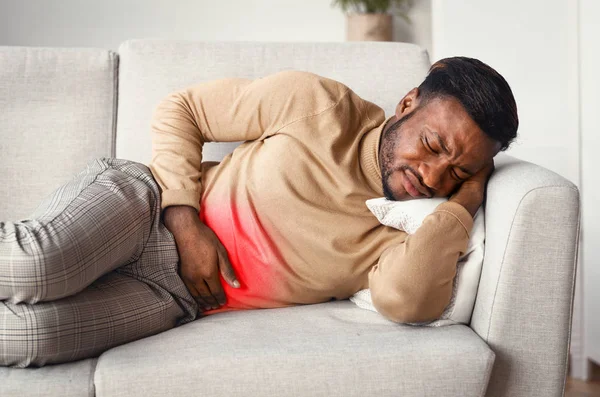 男はソファの上に横たわる胃の赤い痛みゾーンに触れる — ストック写真