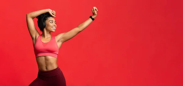 Радостная спортивная девушка в наушниках танцует на красном фоне — стоковое фото