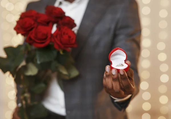 Cultivado de chico negro sosteniendo rosas rojas y anillo de bodas — Foto de Stock
