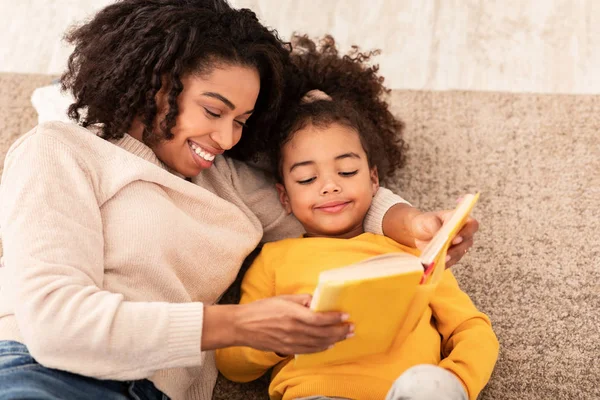 Madre e hija leyendo libro sentado en el sofá en casa — Foto de Stock