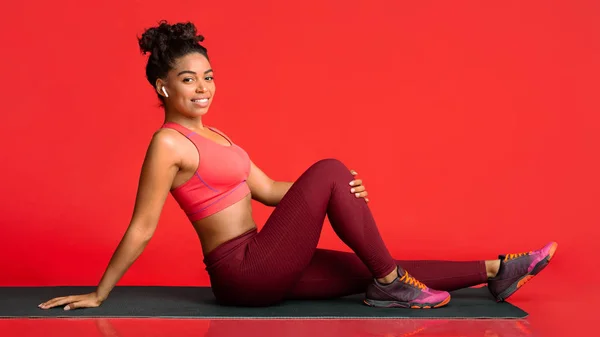 Счастливая фитнес-девушка позирует на коврике для йоги на красном фоне — стоковое фото