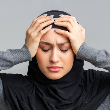 Türbanlı stresli Arap kız elleriyle kafasına dokunuyor.