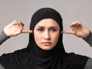 Başörtülü ciddi Müslüman kadın portresi parmaklarıyla kulaklarını kapatıyor.