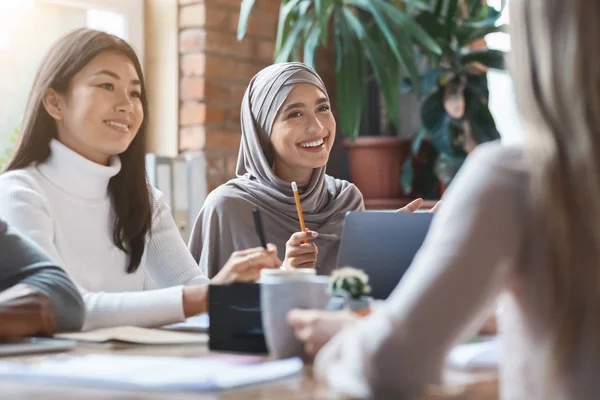 Asiática chica y señora en hijab sonriendo durante reunión de negocios —  Fotos de Stock