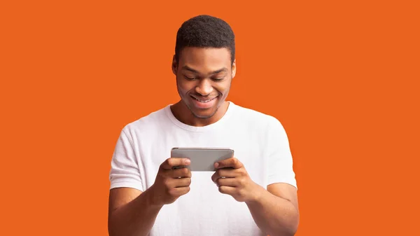 Hombre negro feliz usando teléfono inteligente sobre fondo naranja — Foto de Stock