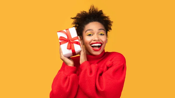 Excited black woman shaking gift box near ear at studio — Stock Photo, Image