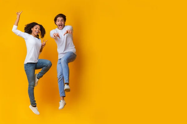 面白い異人種間のカップルは、スタジオで黄色の背景に空気中でジャンプ — ストック写真