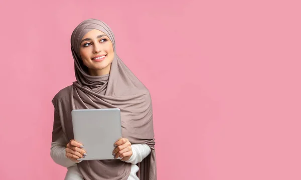Mujer islámica sonriente en pañuelo para la cabeza sosteniendo la tableta digital y mirando a un lado —  Fotos de Stock