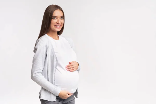 Radostné očekávání žena dotýkající se břicho pózování přes bílé studio pozadí — Stock fotografie