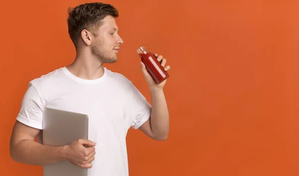 Genç adam dizüstü bilgisayar tutuyor ve kırmızı sağlıklı detoks smoothie içiyor. — Stok fotoğraf