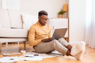 Şok olmuş bir adam laptopta haber okuyor içeride oturuyor.