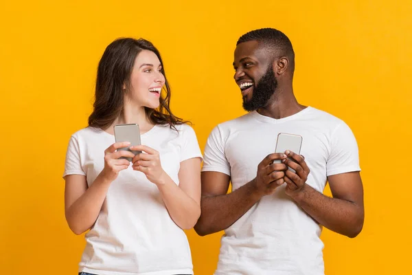Pasangan Jouful antar ras memegang smartphone dan melihat satu sama lain — Stok Foto
