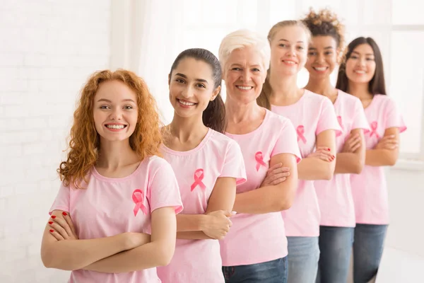 Mesdames en T-shirts avec rubans roses debout sur le mur blanc — Photo
