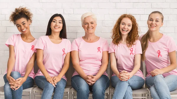 Damer i rosa T-shirts sitter på stolar leende inomhus, Panorama — Stockfoto