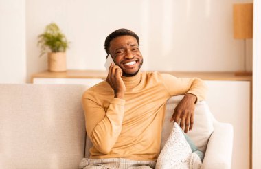 Afrika kökenli Amerikalı Cep telefonuyla konuşan adam, koltukta oturuyor.