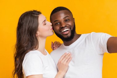 Romantik kız, sarı arka planda selfie çekerken sevgilisini öpüyor.