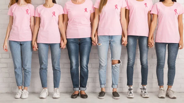 Неузнаваемые женщины в розовых футболках, держащиеся за руки, стоят у стены — стоковое фото