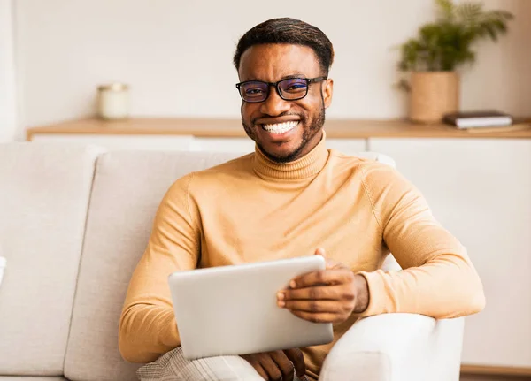 Muž v brýlích drží tabletu sedí na gauči doma — Stock fotografie