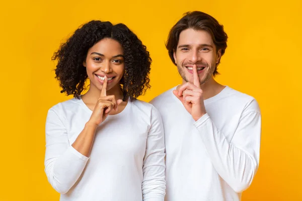 Couple multiracial souriant faisant un geste de silence, cachant un secret — Photo