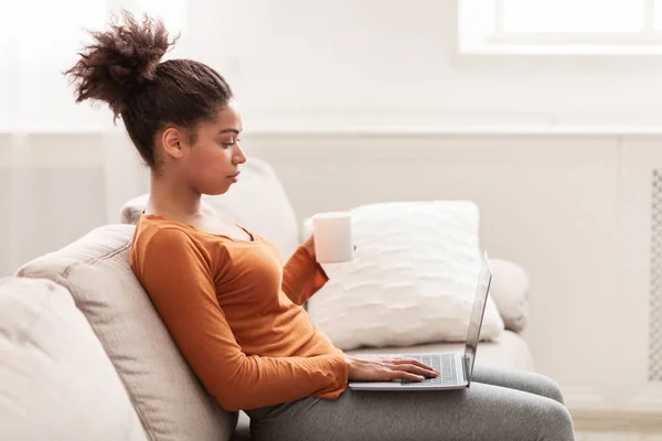Donna seria con computer portatile che lavora seduto sul divano a casa — Foto Stock