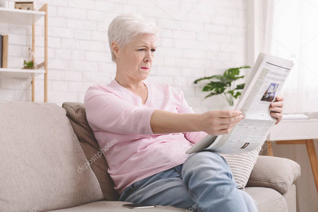 Senior lady squinting and holding newspaper far from eyes