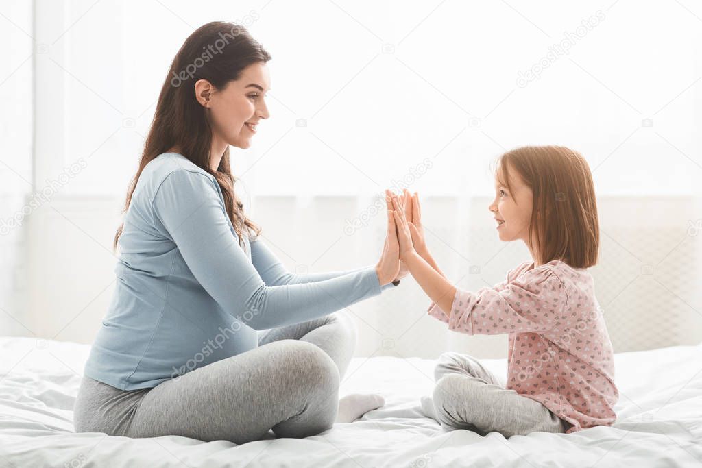 Adorable kid playing with her pregnant mom, sitting on bed