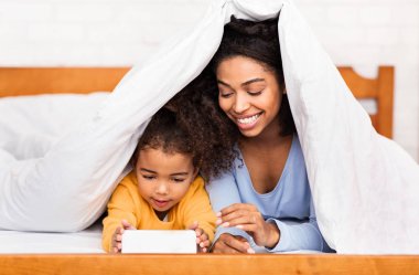 Afrikalı Anne ve Kızı Cep Telefonu Kullanarak Yatakta Yatıyor