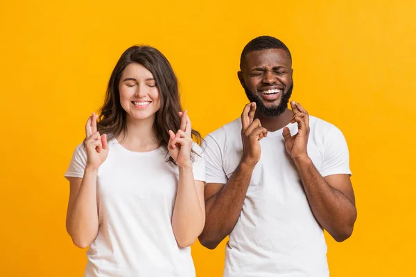 Jóvenes cónyuges multirraciales cruzando los dedos, pidiendo deseos con los ojos cerrados — Foto de Stock