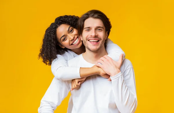 Young interracial couple in love cuddling and posing over yellow background — 스톡 사진