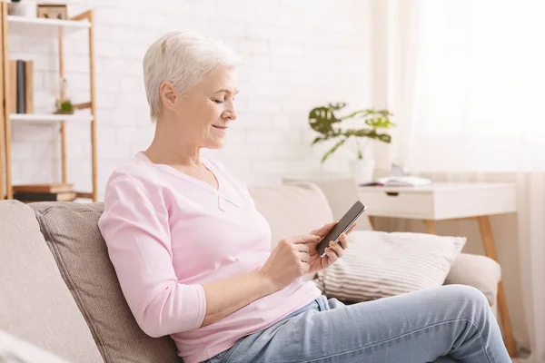 Senior žena chatování na smartphone s přáteli doma — Stock fotografie