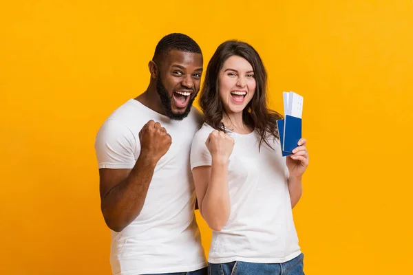 Overjoyed interracial couple holding passports with flying tickets, celebrating getting visa — Stock Photo, Image
