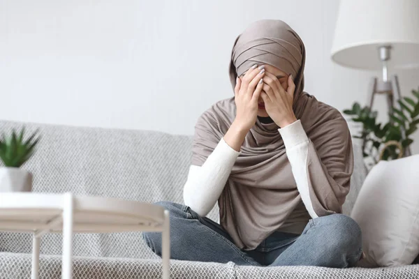 Piangere donna musulmana in hijab seduta sul divano di casa — Foto Stock