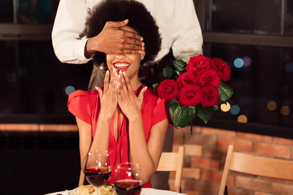 Namorado cobrindo namoradas olhos segurando rosas ter encontro no restaurante — Fotografia de Stock