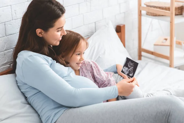 Expecting woman showing ultrasound scan to her daughter — Stock Photo, Image