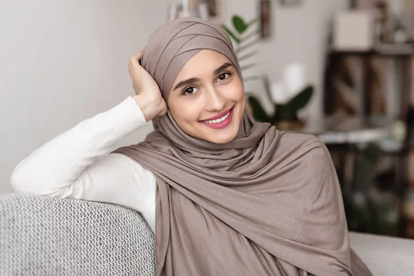 漂亮的阿拉伯女人，头戴头巾坐在沙发上，摆出一副相机的样子 — 图库照片