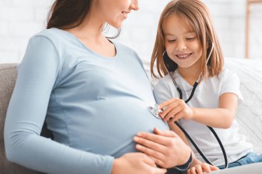 Küçük kız hamile annesiyle doktorculuk oynuyor.