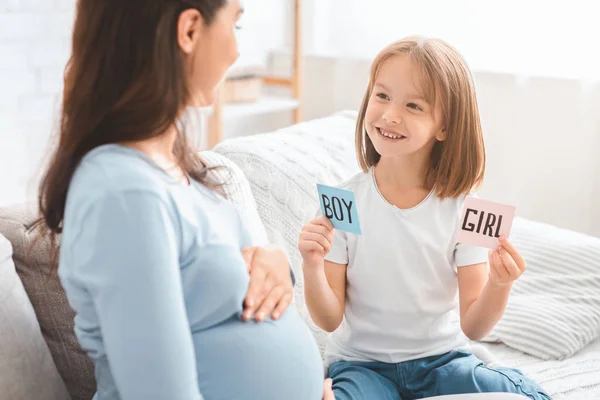 Girl holding pink and blue cards next to mom belly — 스톡 사진