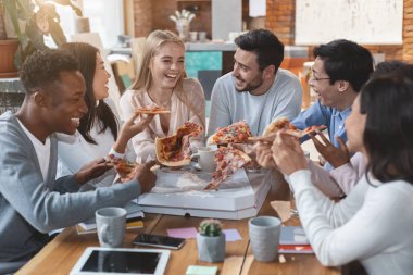 Öğle yemeği saatinde ofiste pizza yiyen mutlu insanlar.