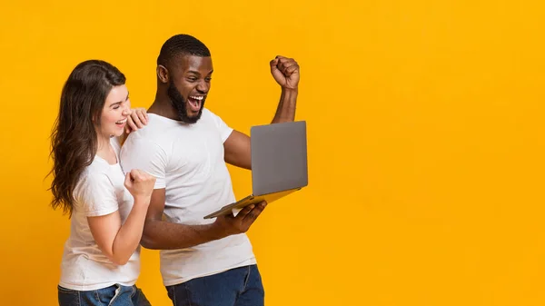 Feliz interracial cónyuges celebrando ganar con el ordenador portátil, levantando los puños en la emoción — Foto de Stock