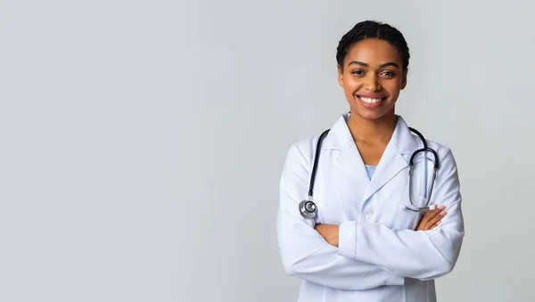 Lächelnde schwarze Ärztin im weißen Mantel posiert mit verschränkten Armen — Stockfoto