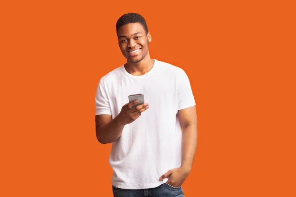 Sonriente hombre negro usando el teléfono celular mirando a la cámara — Foto de Stock