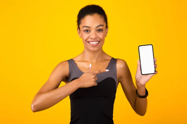 Apto menina apontando dedo mostrando tela do smartphone sobre fundo amarelo — Fotografia de Stock