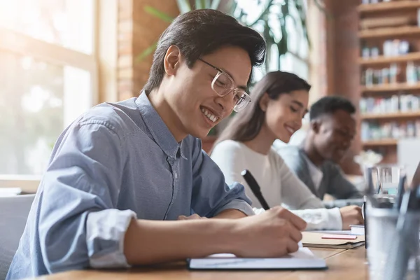 Junger asiatischer Kerl macht sich Notizen, hat Geschäftstreffen mit Kollegen — Stockfoto