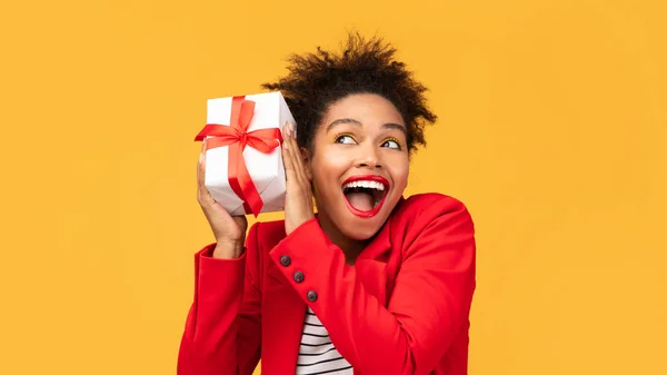 Happy black girl shaking gift box near ear — Stock Photo, Image