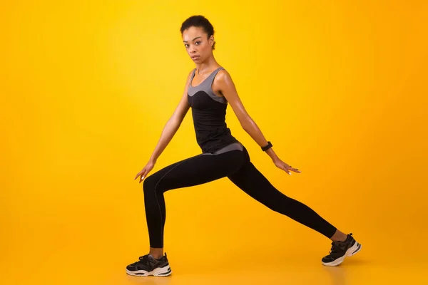 Africano donna fare affondare esercizio Stertching gambe oltre giallo sfondo — Foto Stock