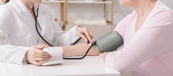 Médico midiendo la presión arterial del paciente mayor en la clínica —  Fotos de Stock