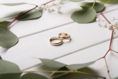 Ahşap arka planda yapraklı bir çift altın alyans.