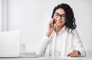 Latin iş kadını telefonla konuşuyor ve yazıyor.