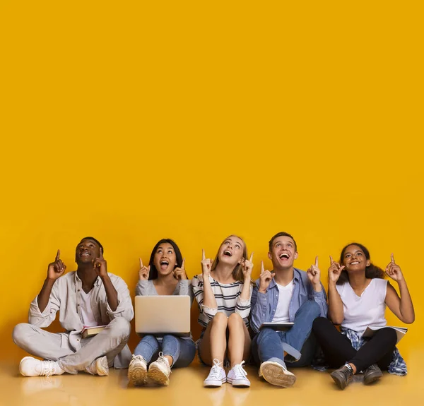 Excited multiracial students pointing up at copy space — ストック写真