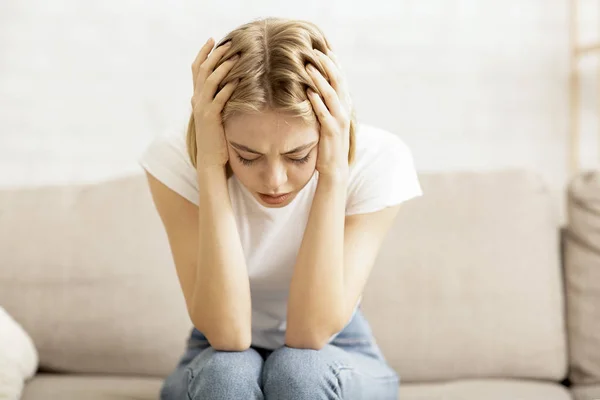 Lonely depressed girl sitting on couch at home — Stock Photo, Image